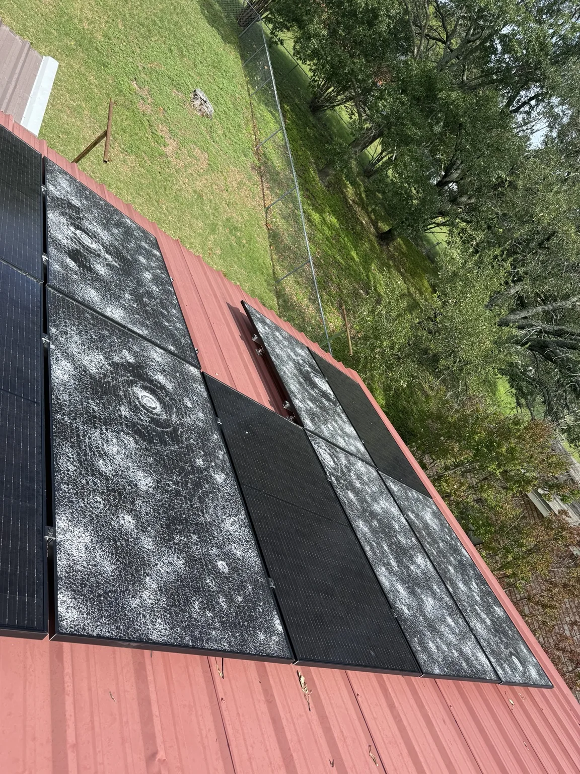 A second view of cracked solar panels on a red metal roof