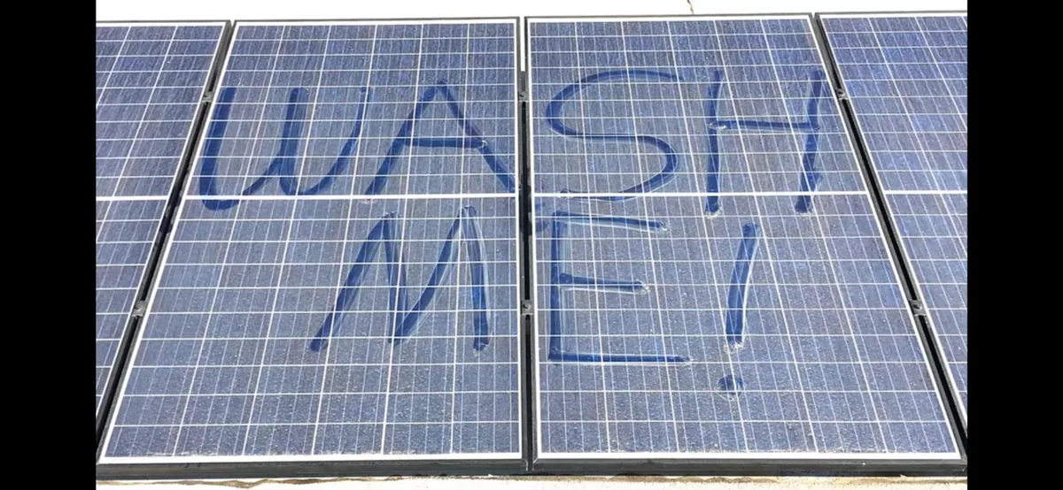 Dust-covered solar panels with wash me written across the surface