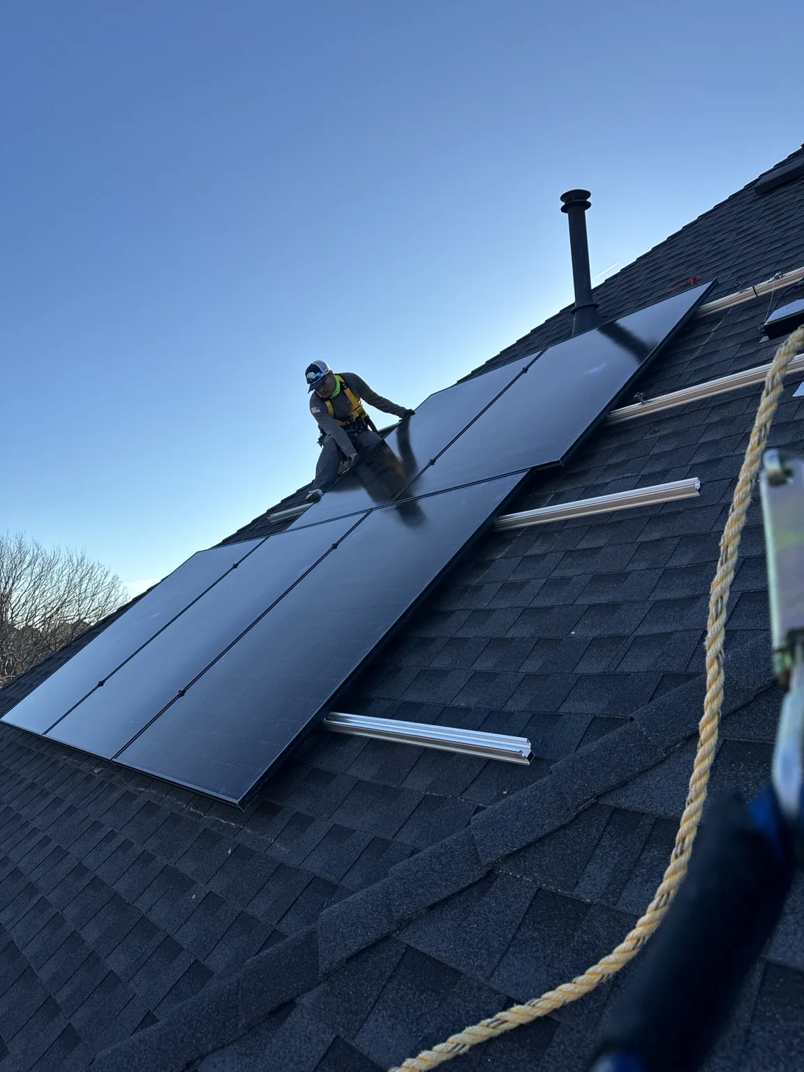 Worker beside solar panels on a pitched shingle roof