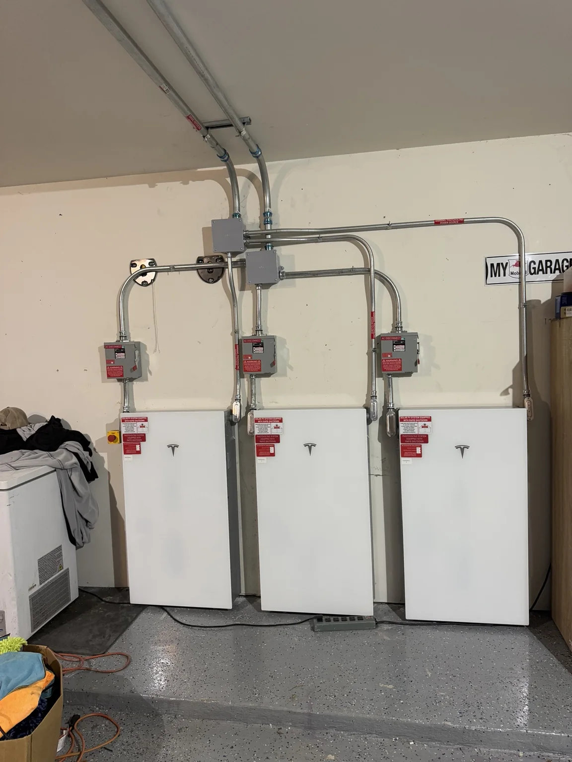 Three battery units with conduit mounted along a garage wall