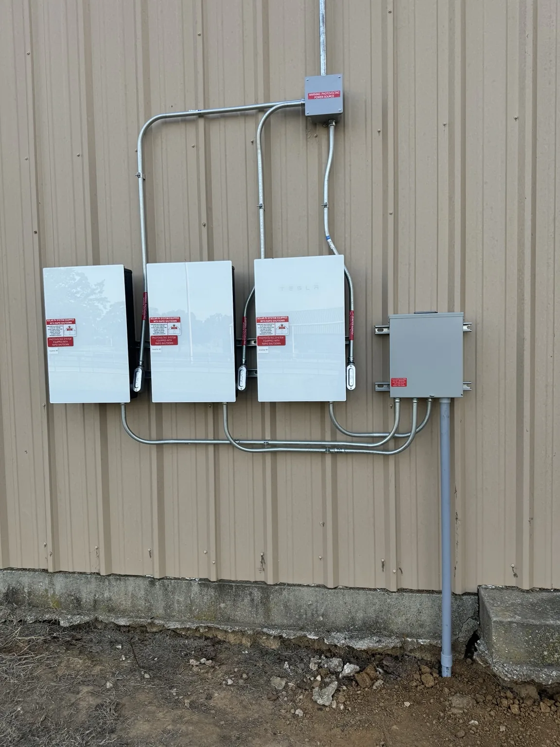 Three exterior solar inverters with conduit on a metal wall